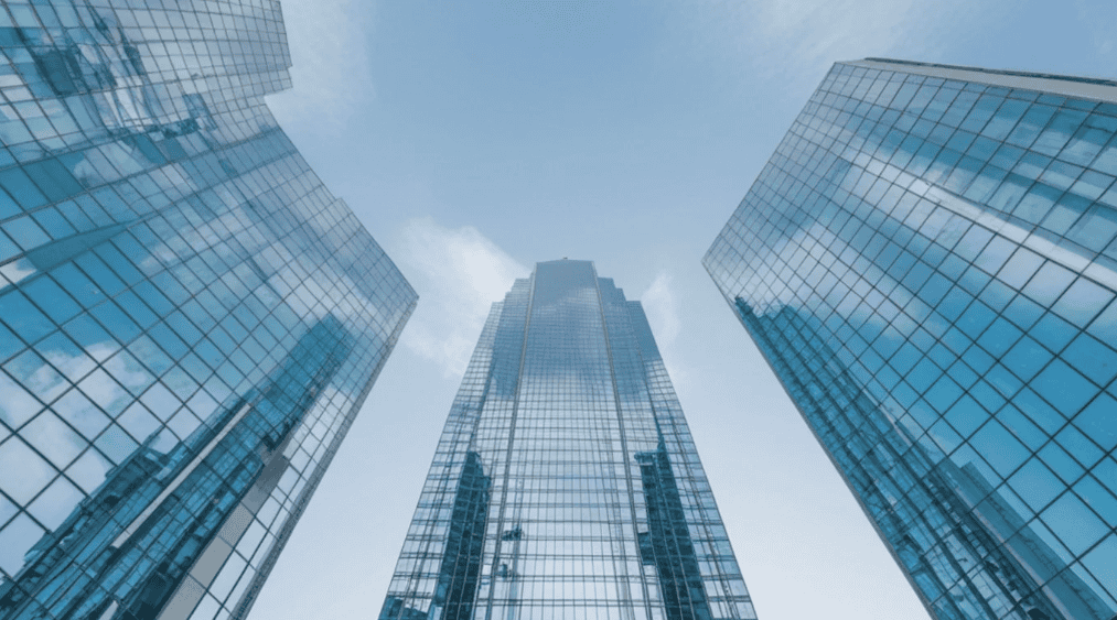 Low-angle view of three blue glass skyscrapers reflecting the sky and clouds.