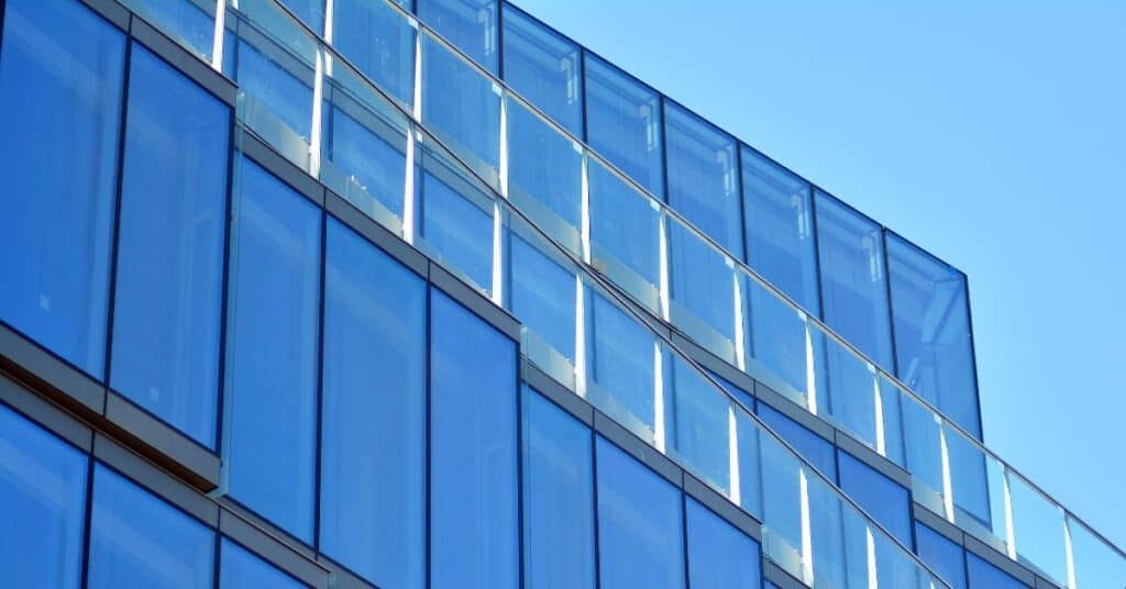 Close-up of a modern building facade with blue-tinted glass panels and glass balconies against a clear blue sky.