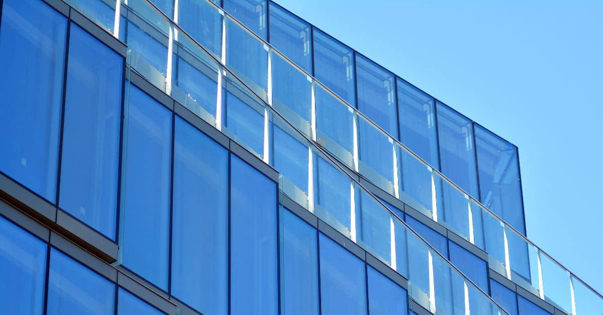 Close-up of a modern building facade with blue-tinted glass panels and glass balconies against a clear blue sky.