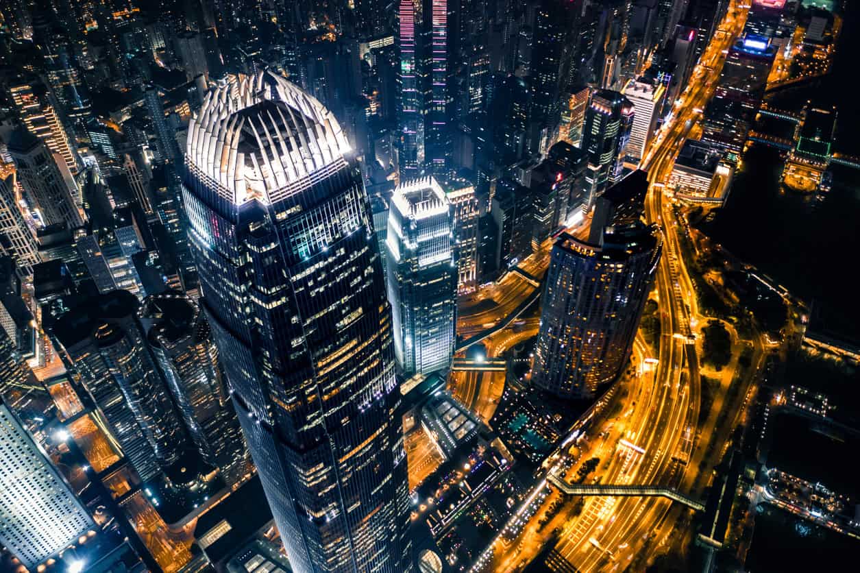Aerial view of a brightly lit city at night, featuring numerous skyscrapers and glowing road networks.