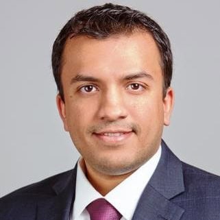 Headshot of a man in a dark suit and purple tie smiling.