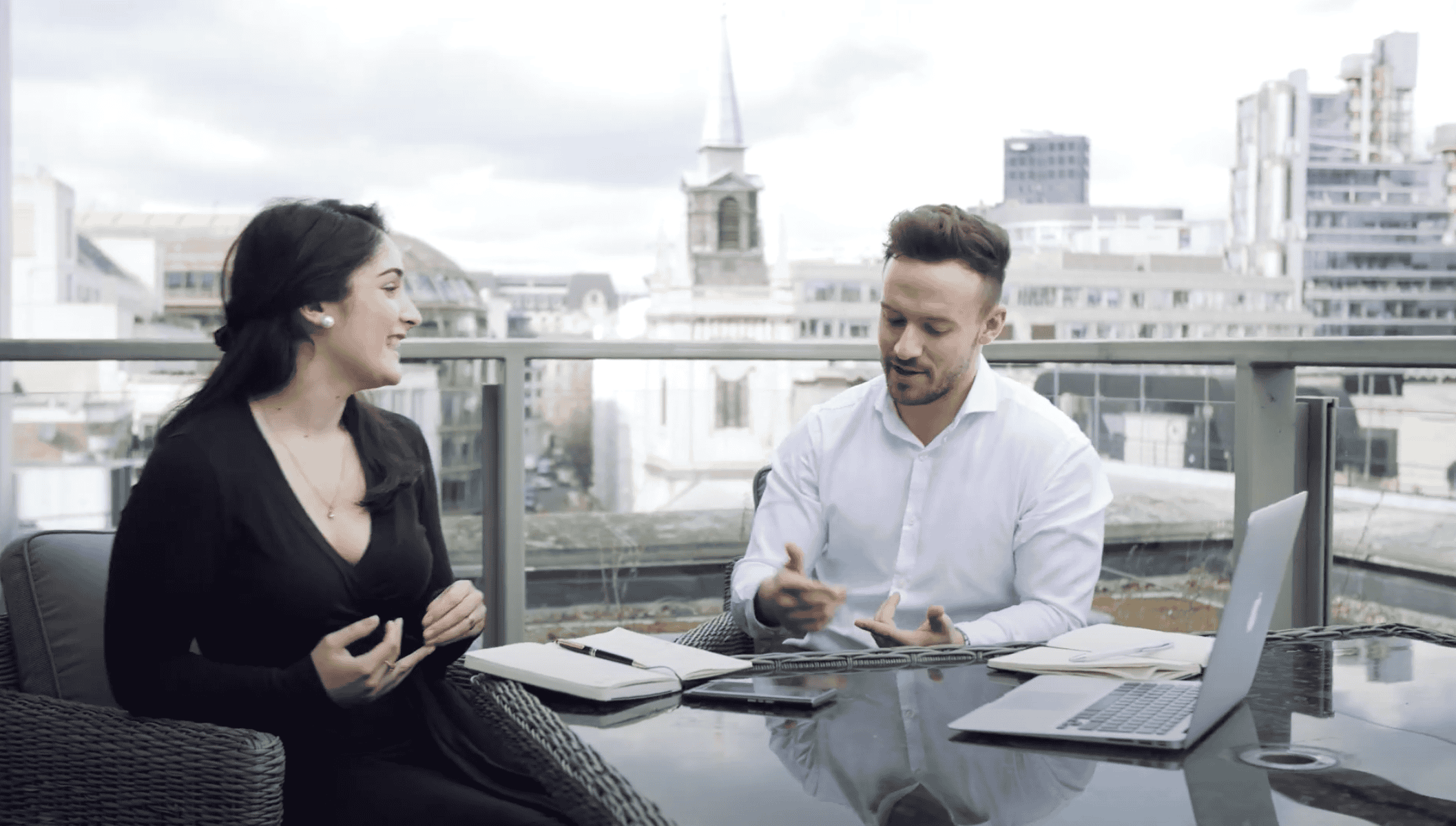 A screenshot of a web browser displaying a YouTube video of a man and a woman discussing careers on a rooftop patio with a city skyline in the background.