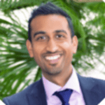 Headshot of a smiling man in a suit and tie against a blurred green background.