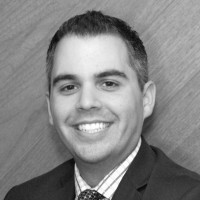 Black and white headshot of a smiling man in a suit and tie.