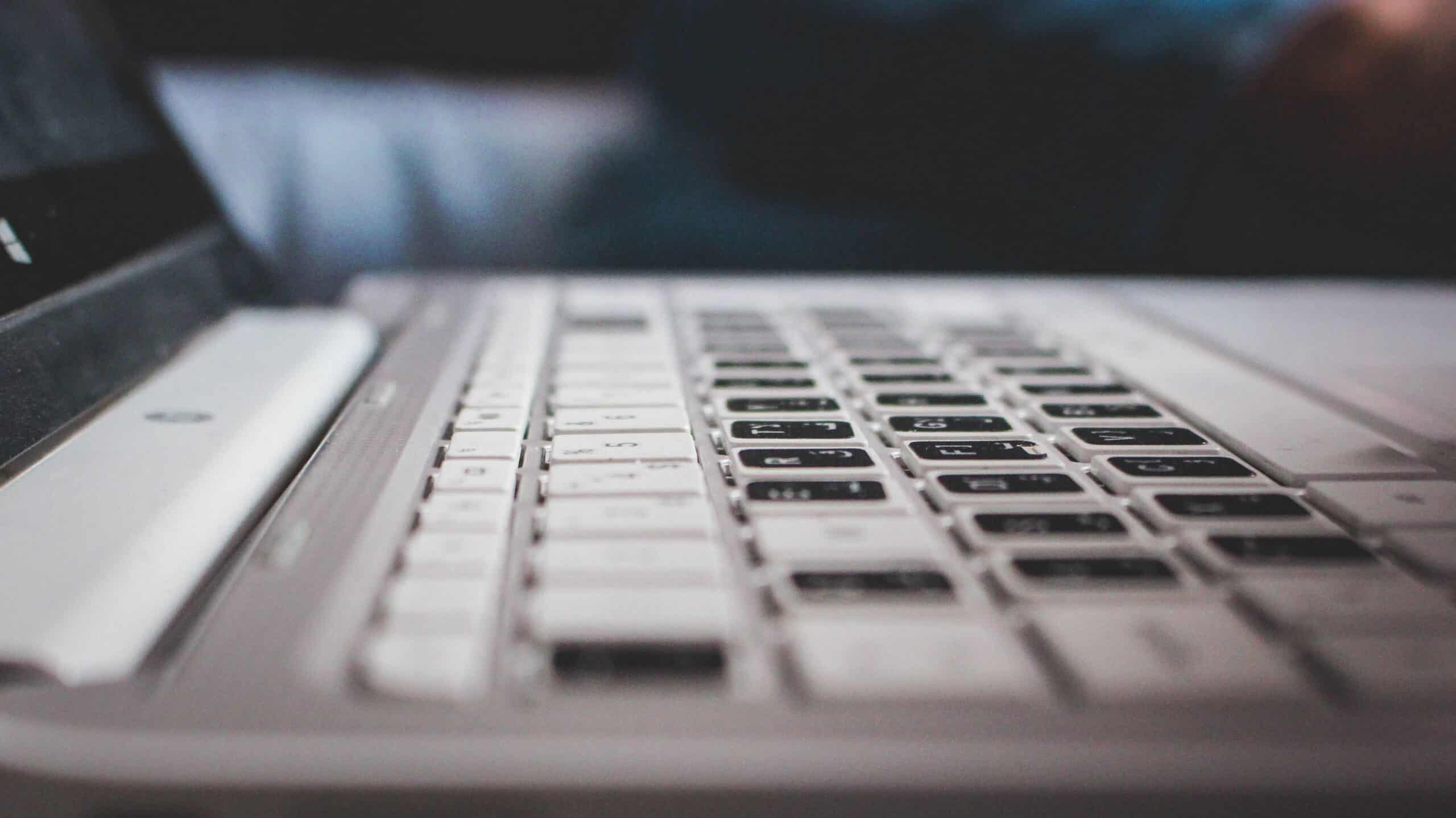 Close-up of a laptop keyboard with light-colored keys and dark characters, viewed from a low angle.