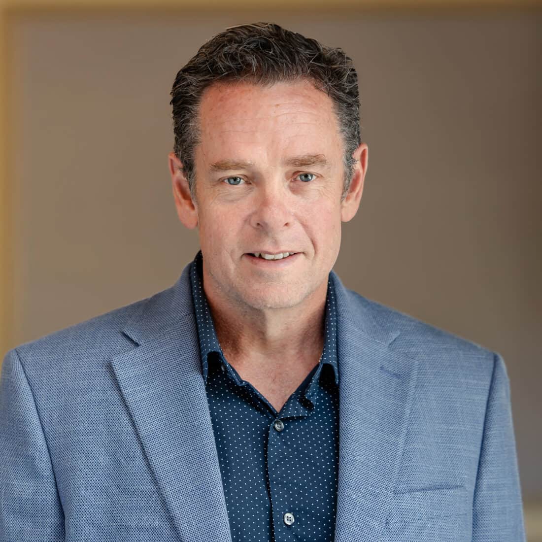 Headshot of a man in a blue blazer and dark polka dot shirt.