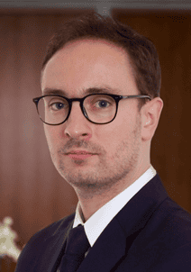 Headshot of a man with dark hair, glasses, and a suit looking forward.