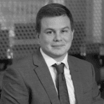 Black and white portrait of a man in a suit and tie, smiling.