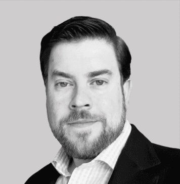 Black and white headshot of a man with dark hair and a beard, wearing a collared shirt and jacket.