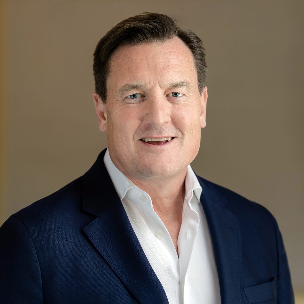 Headshot of a smiling man in a navy suit jacket and white shirt.