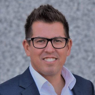 Headshot of a smiling man in a suit and black-framed glasses.