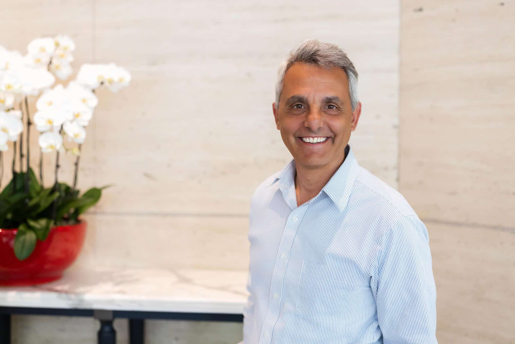 A smiling middle-aged man in a striped shirt, with white orchids in the background.