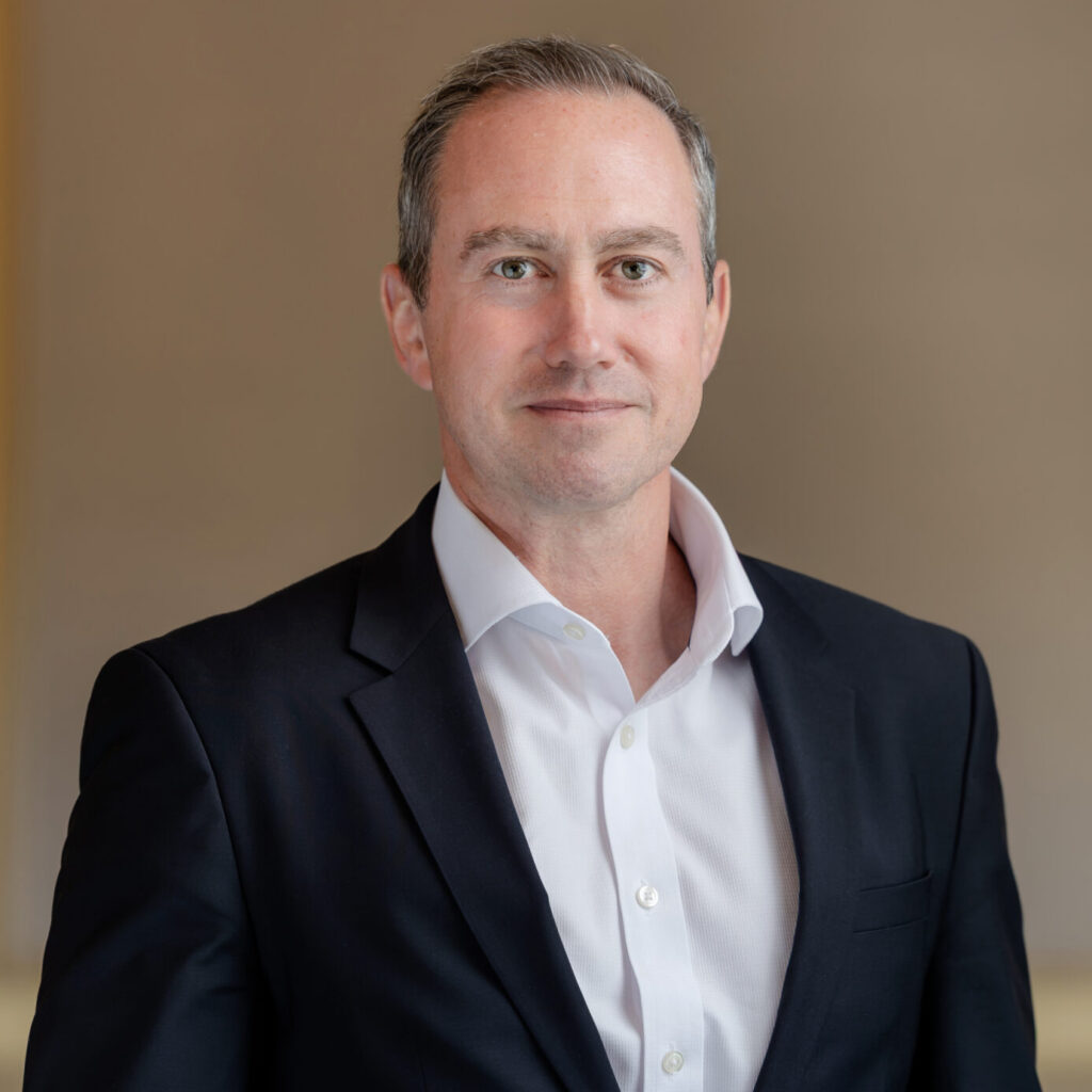 A man in a dark suit and white shirt looks directly at the camera in a professional headshot.