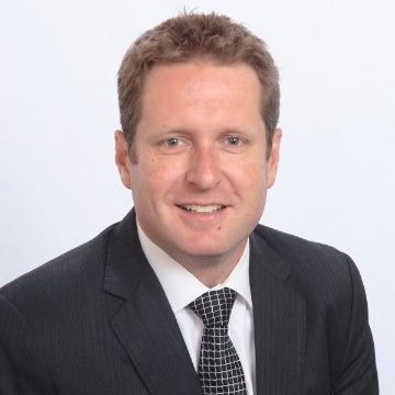 Headshot of a man with light brown hair, wearing a dark suit and checkered tie, smiling.