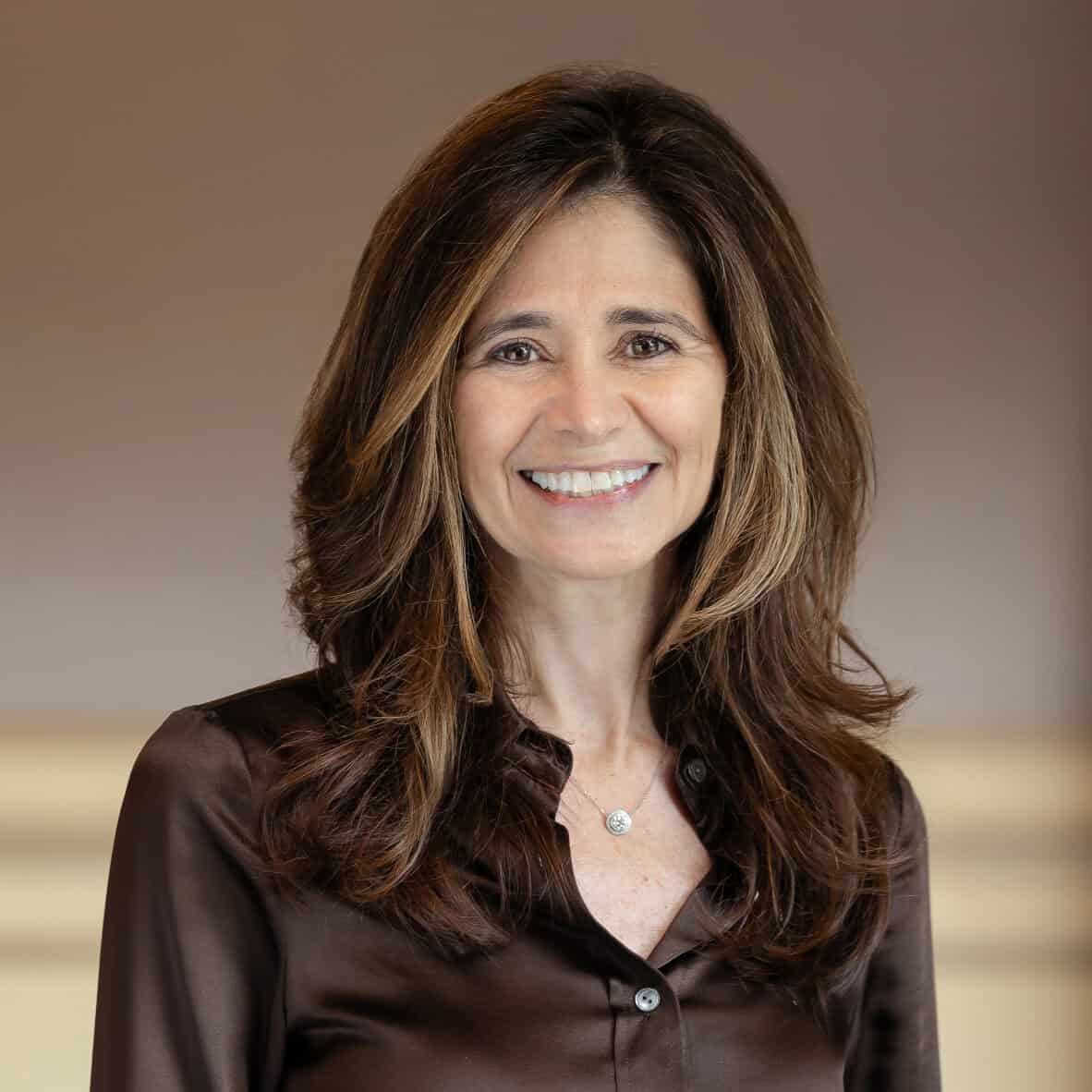 Headshot of a smiling woman with long brown hair wearing a brown satin blouse and a silver necklace.