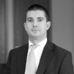 Black and white headshot of a man in a suit and tie, looking forward.