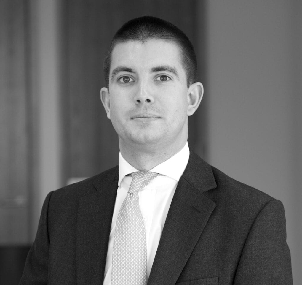 Black and white headshot of a man in a suit and tie, looking forward.