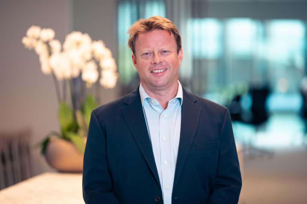 Portrait of a smiling man with light brown hair, wearing a dark blue blazer and light blue shirt.