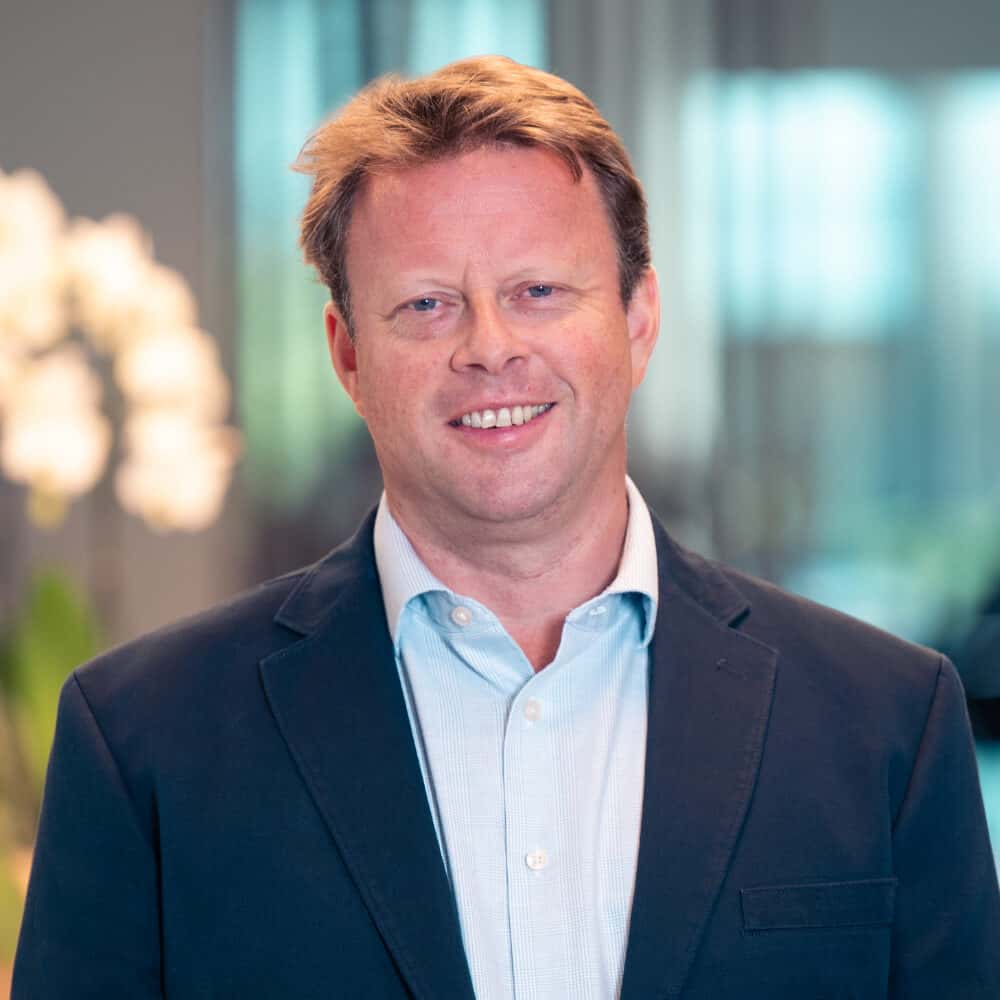 Portrait of a smiling man with light brown hair, wearing a dark blue blazer and light blue shirt.