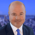Headshot of a bald man in a suit and tie with a blurred city background.