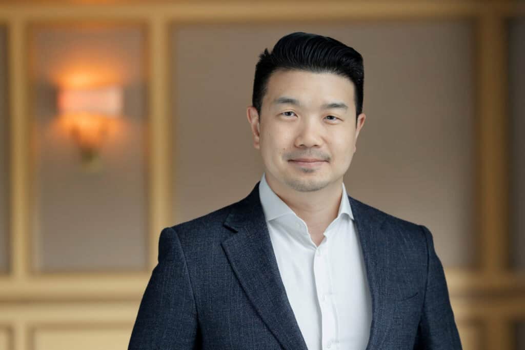 Headshot of an East Asian man in a dark suit jacket and white shirt, looking at the camera with a slight smile.