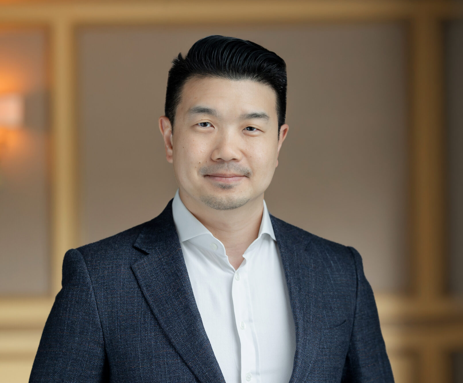 Headshot of an East Asian man in a dark suit jacket and white shirt, looking at the camera with a slight smile.