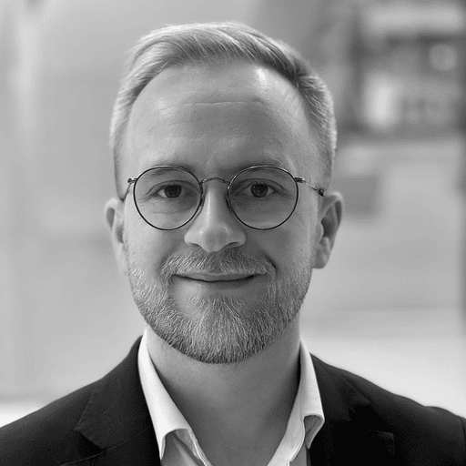 Black and white headshot of a smiling man with a beard and round glasses.