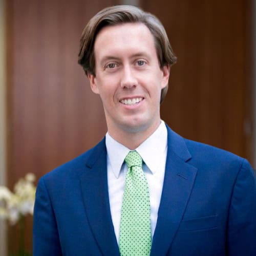 Headshot of a smiling man with light brown hair, wearing a blue suit and a light green polka dot tie.
