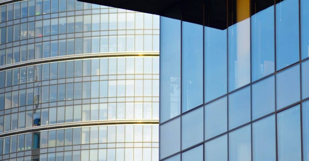 Close-up of two modern glass buildings, one curved with golden bands and the other angular with blue reflections.