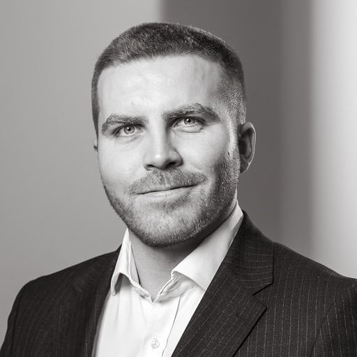Black and white headshot of a man with short hair and a beard, wearing a pinstripe suit and white shirt, smiling slightly.