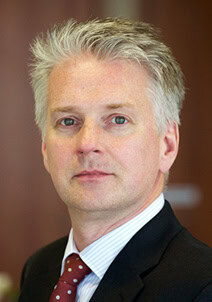 Headshot of a man with graying hair, wearing a dark suit, striped shirt, and red polka dot tie.