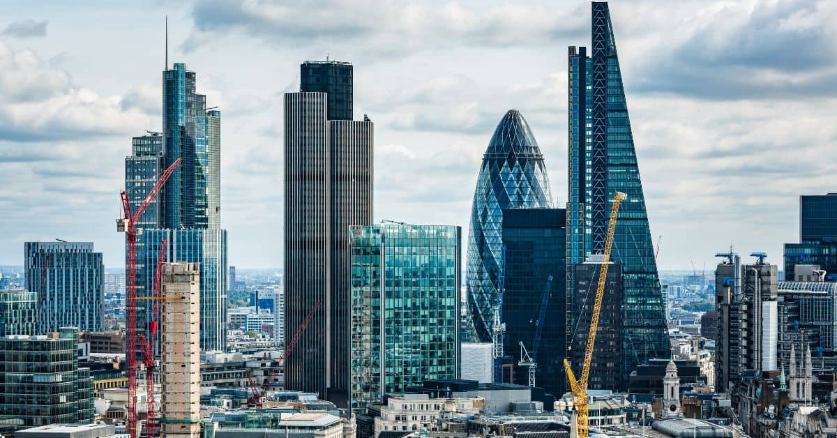 A city skyline featuring numerous modern skyscrapers, including The Gherkin, and several construction cranes under a cloudy sky.
