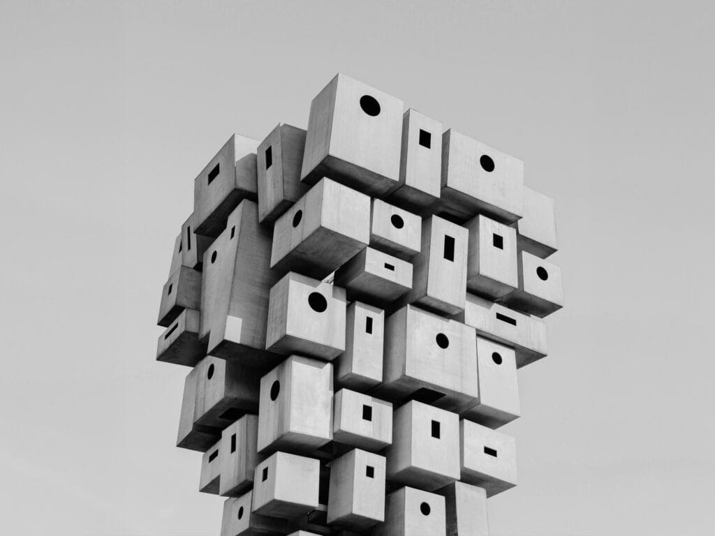 Black and white image of an abstract sculpture made of many stacked and cantilevered rectangular boxes with circular, square, and rectangular openings.