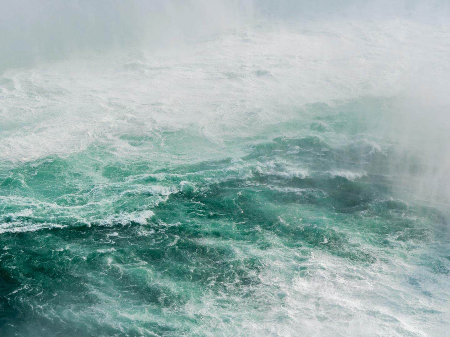 A close-up view of turbulent, green and white water with heavy mist and spray.