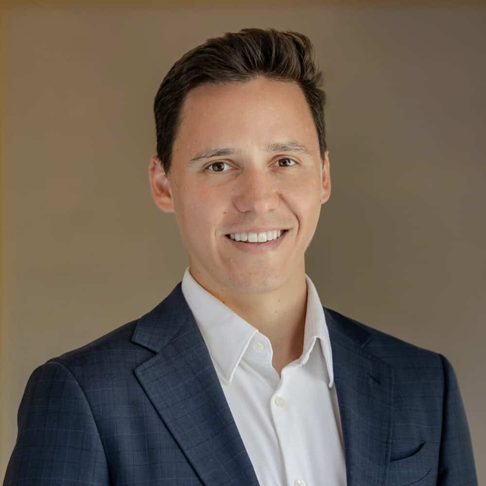 Headshot of a smiling man with dark hair wearing a blue plaid suit jacket and white shirt.