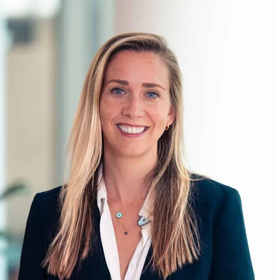 Headshot of a smiling woman with long blonde hair, blue eyes, wearing a dark blue blazer and white shirt.