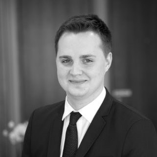 Black and white headshot of a young man in a suit and tie, smiling.