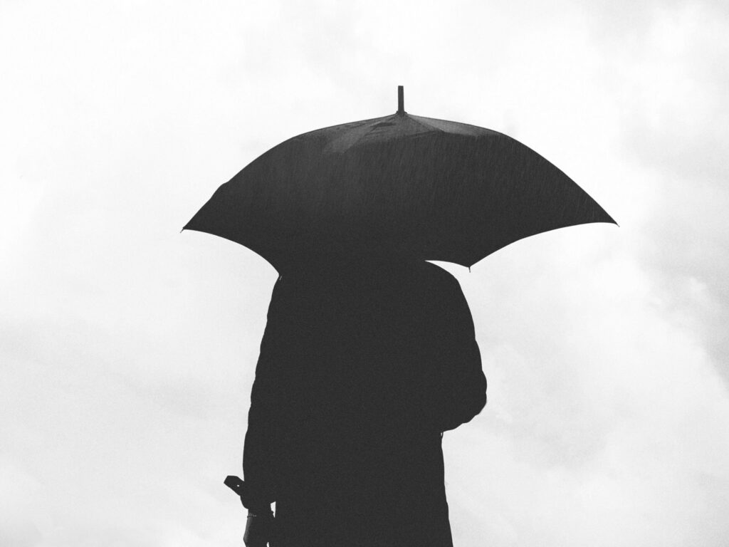 Black and white silhouette of a person holding an umbrella in the rain.