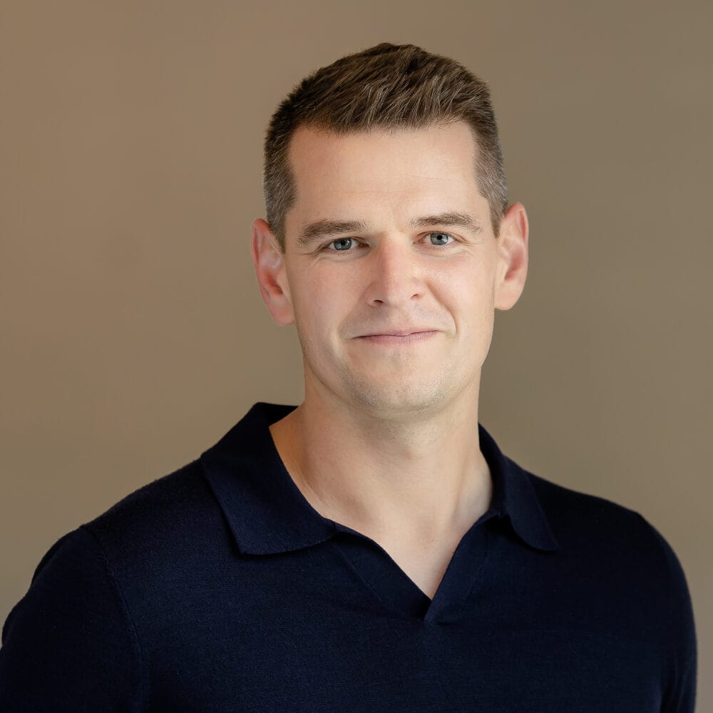 A man with short dark hair and a dark blue polo shirt smiles at the camera.