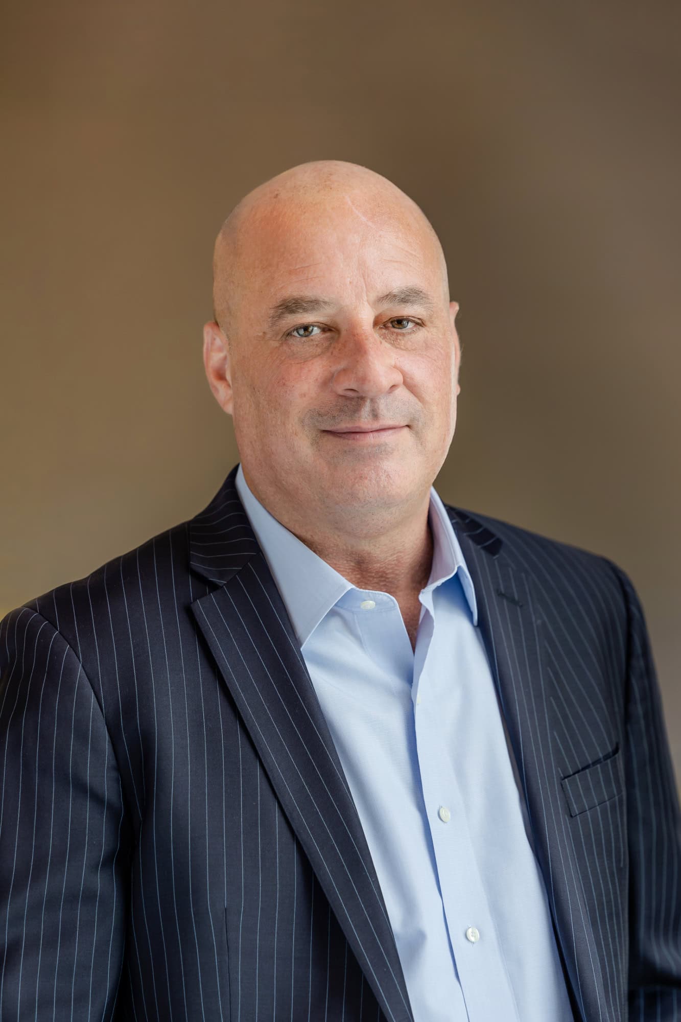 Headshot of a bald man with a slight smile, wearing a dark pinstripe suit and light blue shirt.