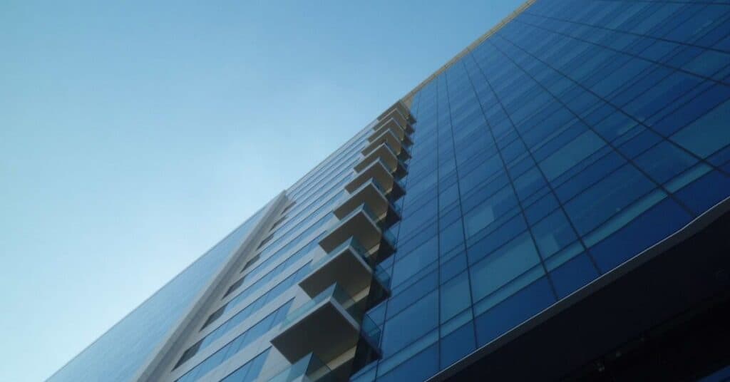 Low-angle view of a modern skyscraper with blue glass facade and stacked balconies against a clear blue sky.