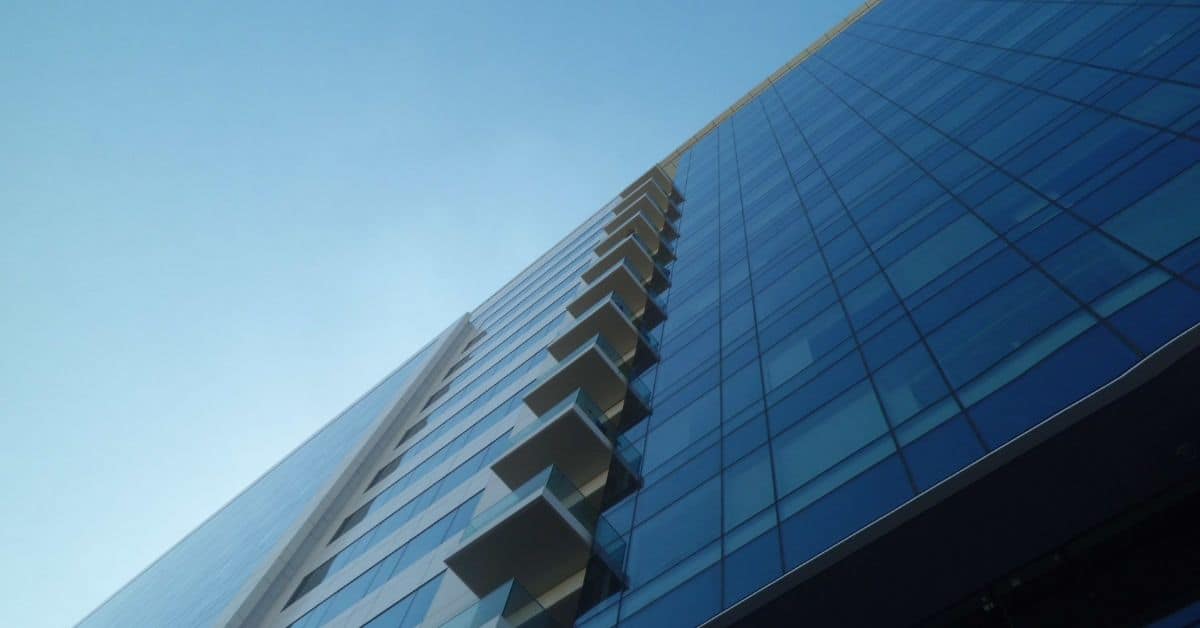Low-angle view of a modern skyscraper with blue glass facade and stacked balconies against a clear blue sky.