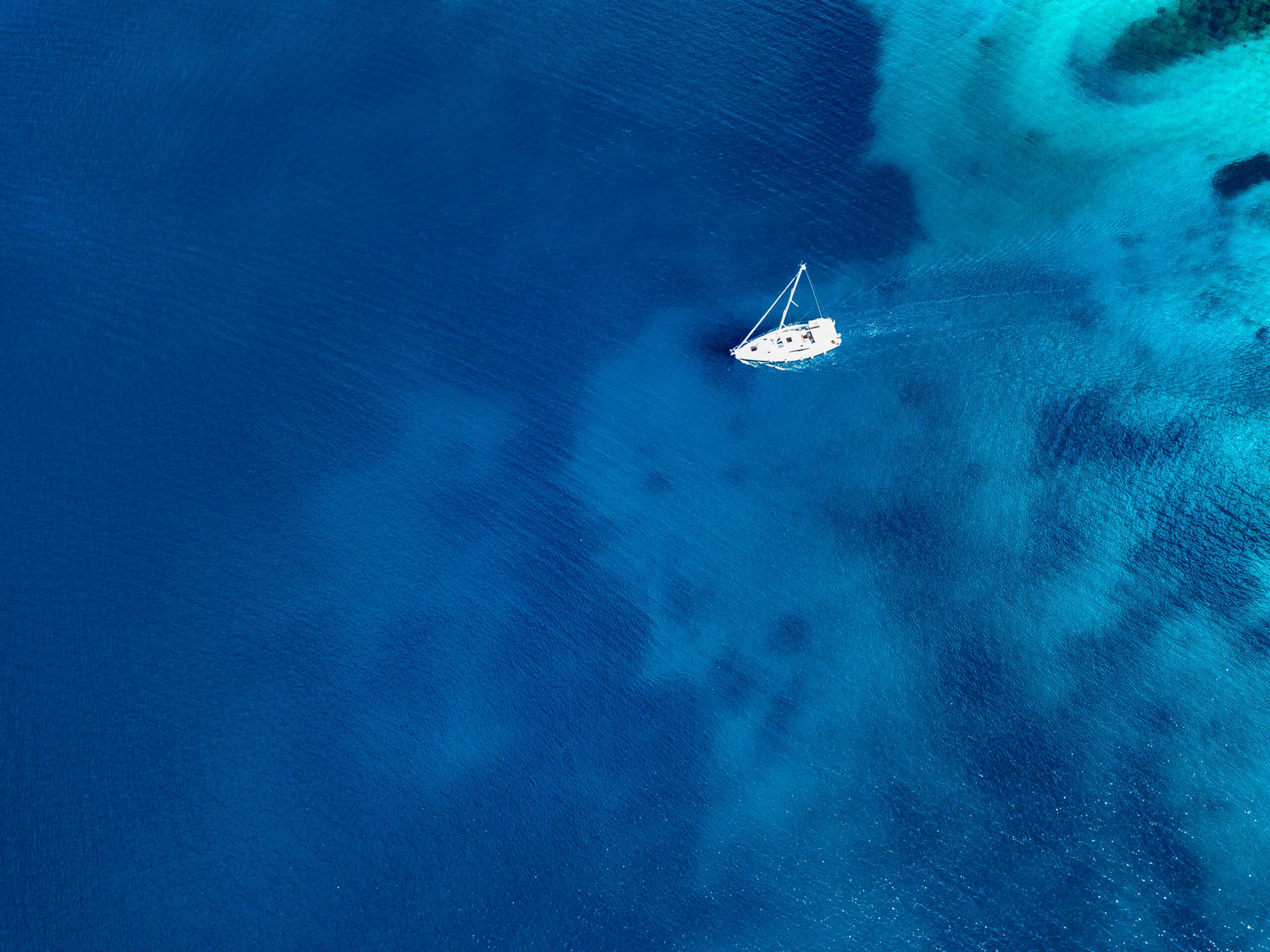 Aerial view of a white sailboat on clear blue and turquoise ocean water.