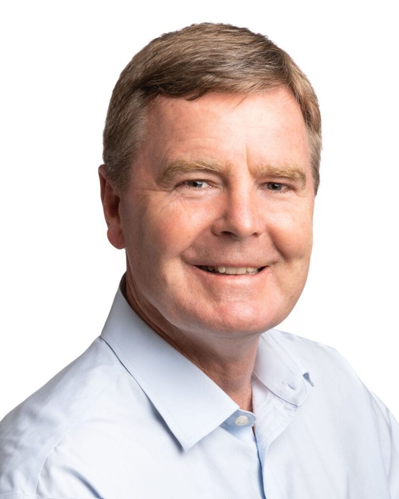 Headshot of a smiling man with light brown hair wearing a light blue collared shirt.