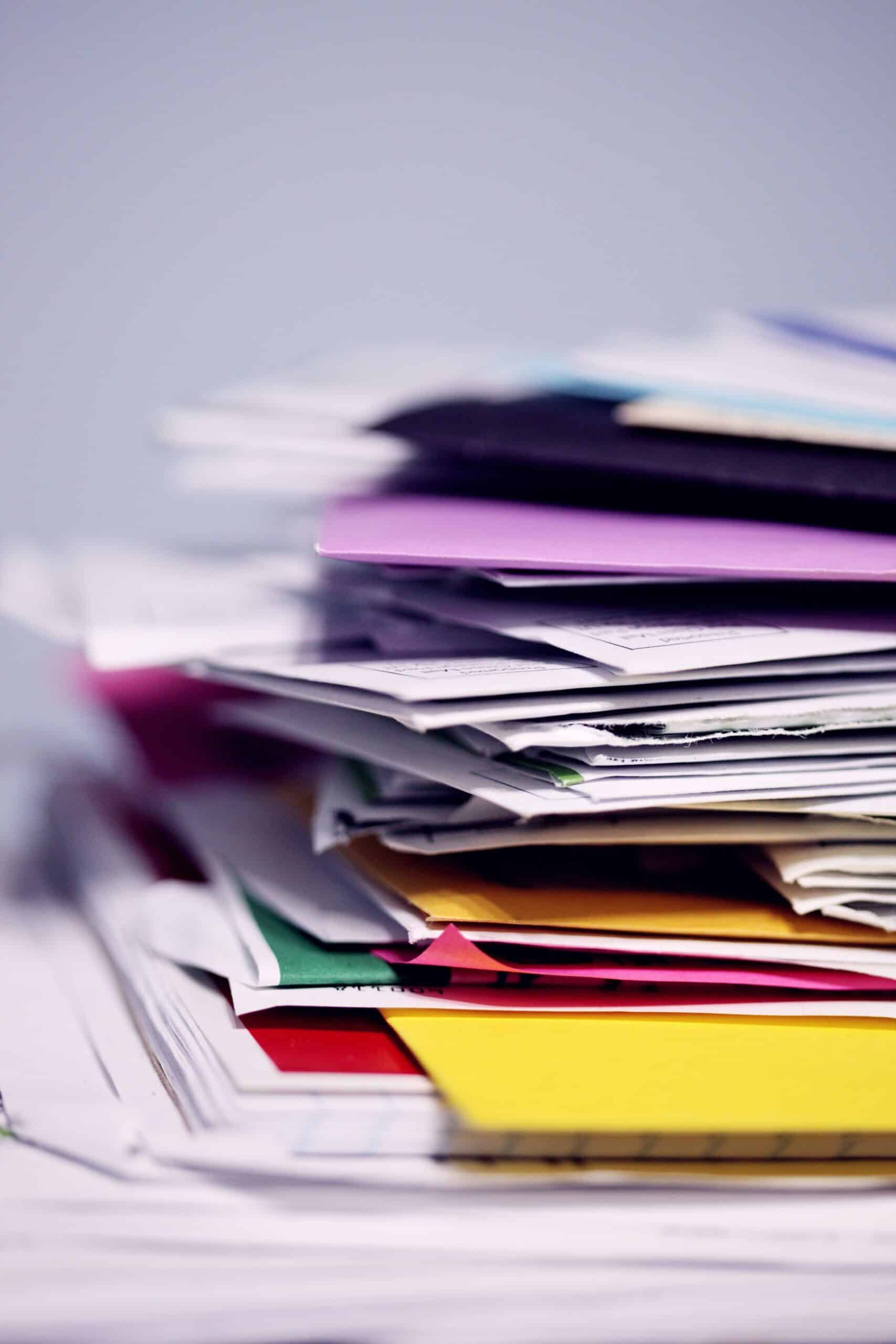 A large, messy stack of colorful papers and folders, shot from a low angle.