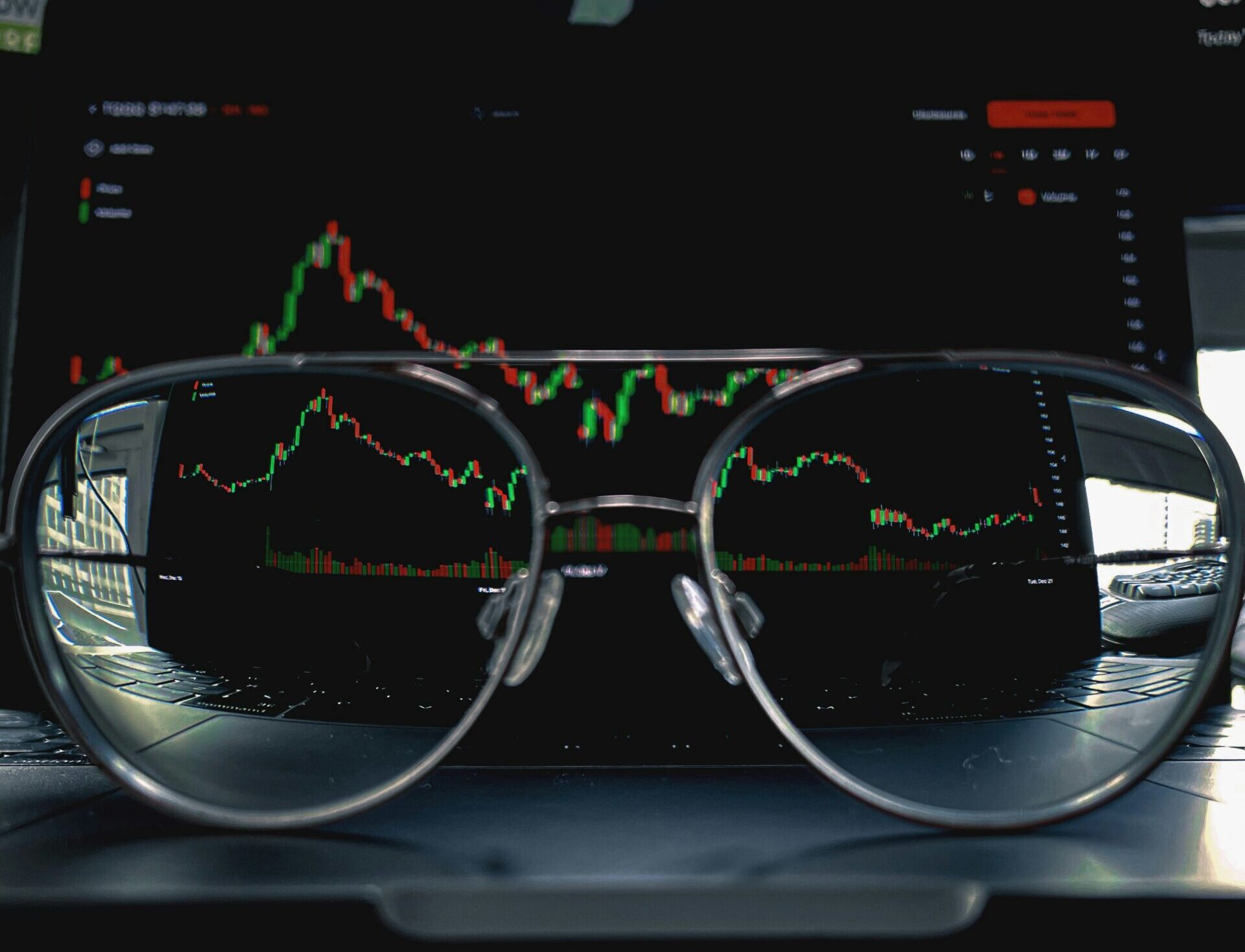 Eyeglasses on a laptop keyboard, reflecting a financial candlestick chart on the screen.